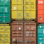 Tumpukan peti kemas berwarna-warni di pelabuhan sebagai gambaran aktivitas impor ekspor global