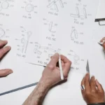 Dua orang berkolaborasi mengerjakan desain produk di atas meja kerja